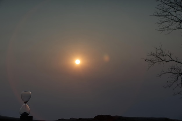 An hourglass (with falling sand) with sea of fog and mountain range silhouette in sunrise time