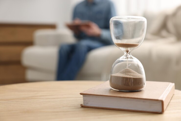 Photo hourglass with flowing sand on desk man reading book in room selective focus