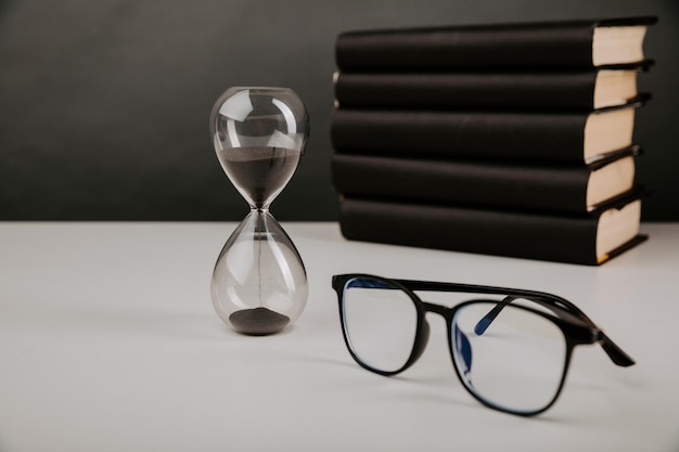 Hourglass with glasses and books on a desk