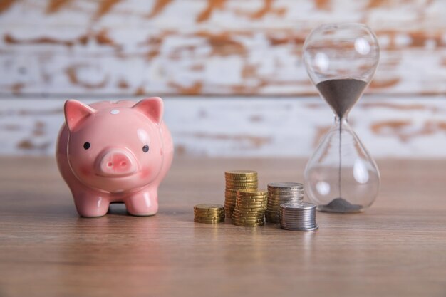 Hourglass with piggy bank and coins on tablexA