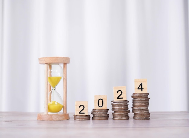 Photo hourglass and wooden block with number 2024 on stack of coins the concept of saving money manage time to success financial investment and business growing in new year 2024