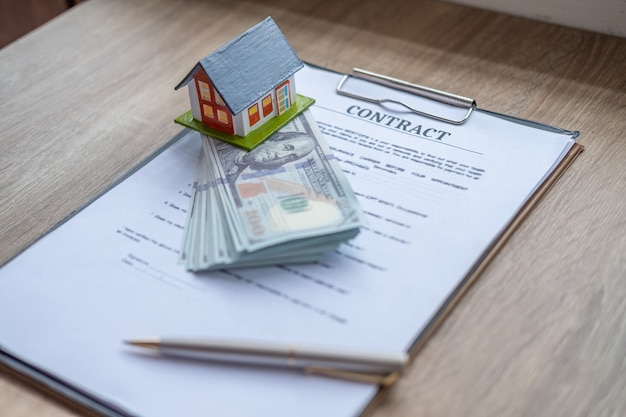 Photo house buying concepts, small house model and money with document contract and pen on wooden table.