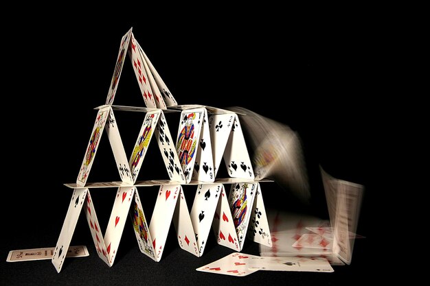 Photo house of cards collapsing on dark backgroun