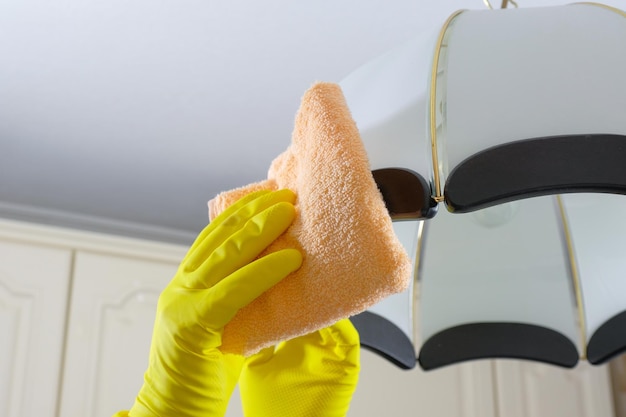 House cleaning closeup of gloved hands cleaning a chandelier\
with a rag