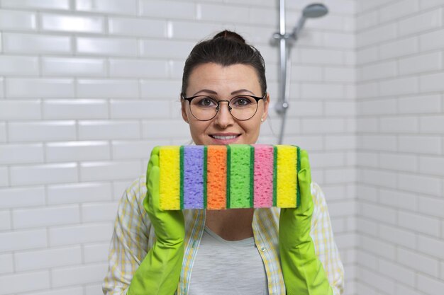 House cleaning concept. Woman in protective gloves holding many cleaning sponges, background bathroom interior, white ceramic tile