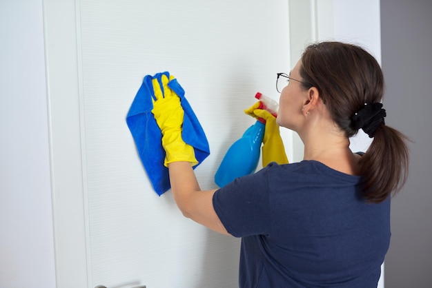 Photo house cleaning mature woman cleans at home in living room in yellow gloves with spray cleans white interior door hygiene purity cleanliness concept