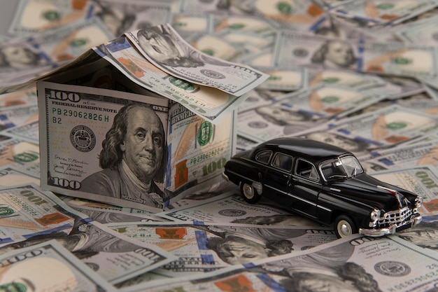 Photo a house of dollar bills and a car on scattered bills