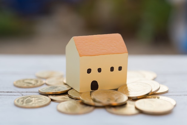 House and  golden coins on wooden table with blurred nature,properties concept