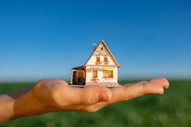 House in hand against spring green field and blue sky surface