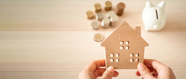 A house held on the hands of a woman planning to save money to invest in real estate. For saving or investing for a home.