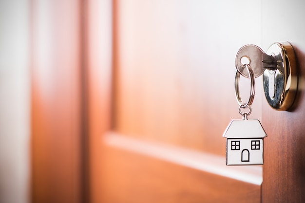 House key on a house shaped silver keyring in the lock of a entrance  brown door