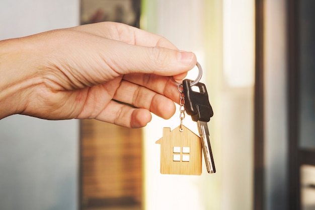 House key in male hand at apartment background. house key ring. Concept of moving in new living apartment. Symbol of purchasing house. Estate investment. Buy property. real estate transaction.