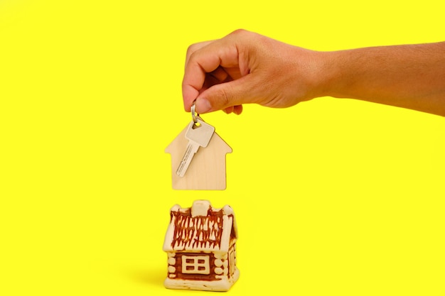 House and key with keychain in your hand on yellow background, selling buying or renting an apartment.