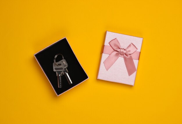 House keys in a gift box with a bow on a yellow background. Housing as a gift. Top view