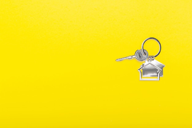 House keys with trinket on color yellow background