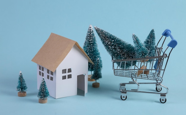 House model and Christmas tree shopping trolley on a blue background