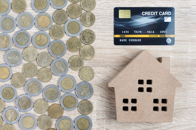 House model and coins arrangement with credit card on wooden table