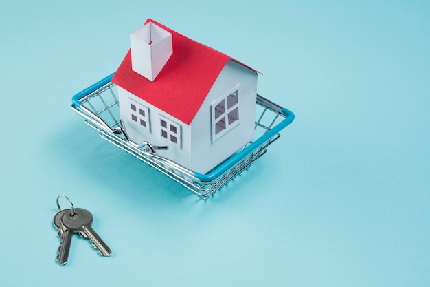 Модель дома в металлической корзине и ключи на синем фоне