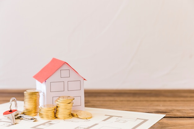 Photo house model, key and stacked coins on blueprint