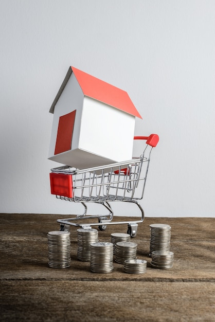 Photo house model in shopping cart and row of coin money