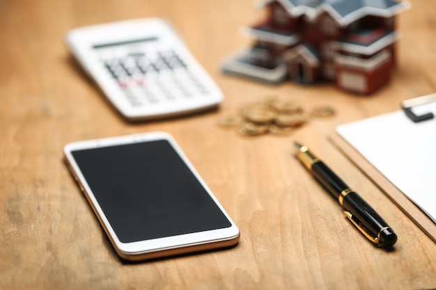 Photo house model ,smartphone ,calculator and golden coins on wooden table