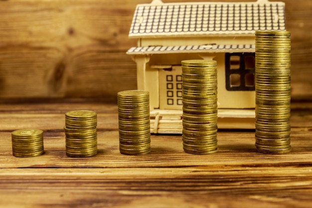 House model and stacks of golden coins on wooden background Property investment home loan house mortgage real estate concept