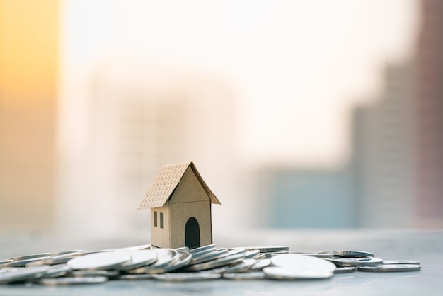 House models on pile of coin with city backgrounds.