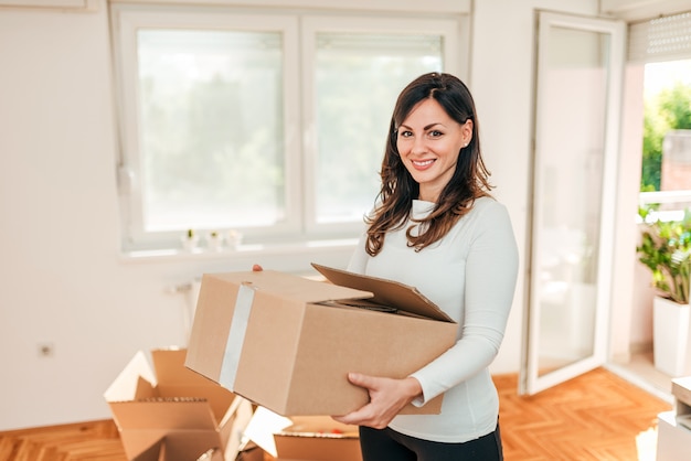 Photo house moving concept. woman holding cardboard box, looking at camera.