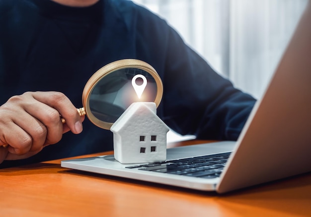 House online search Property value home buying and selling real estate investment concepts Location map pointer icon on white house on laptop while businessman looking by magnifying glass in hand