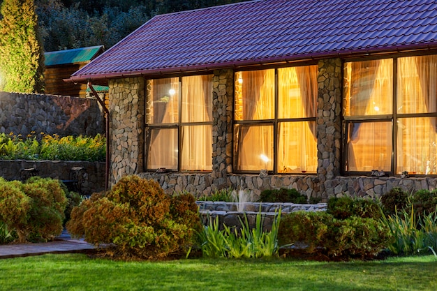 House with luminous windows in the evening on the nature. Cosiness and comfort.