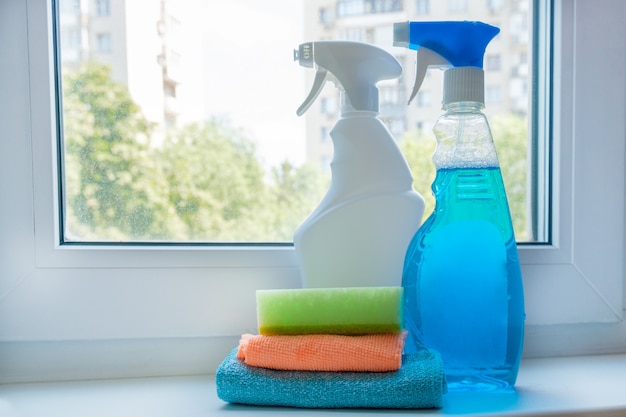 Household chemicals in spray bottle for cleaning windows on windowsill on background of dirty window