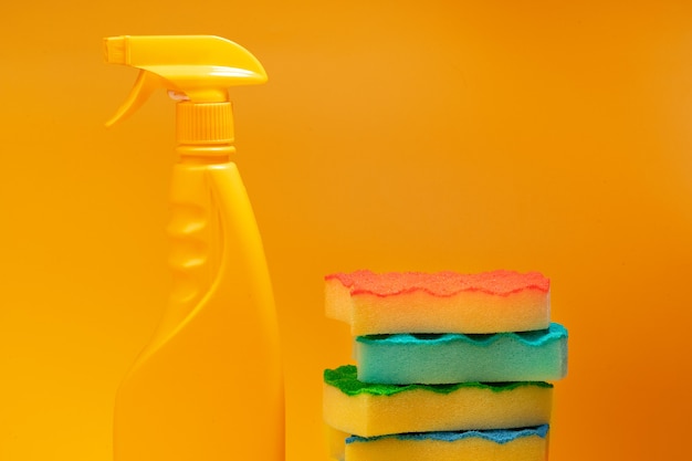 Household cleaning detergents and sponges on yellow background