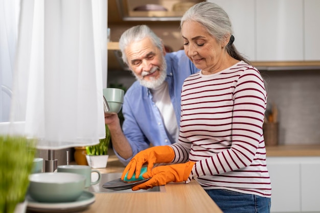 家庭のコンセプト笑顔の年配の夫と妻が台所で一緒に皿を洗う