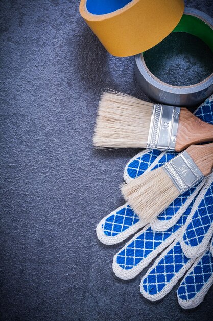 Household tape paintbrushes safety gloves on black background construction concept