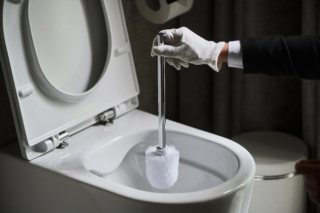 Housekeeper in a neat white apron standing scrubbing out a toilet with a brush