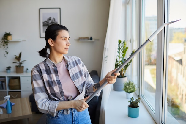 Housekeeper using mop to clean the window in the room at home