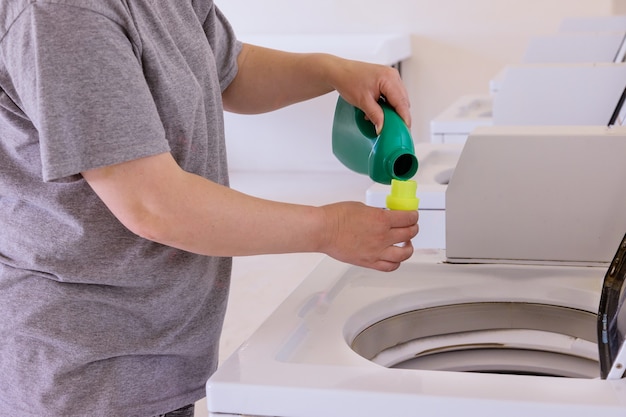 Housekeeper woman pours the liquid powder in washing machine on\
laundry room