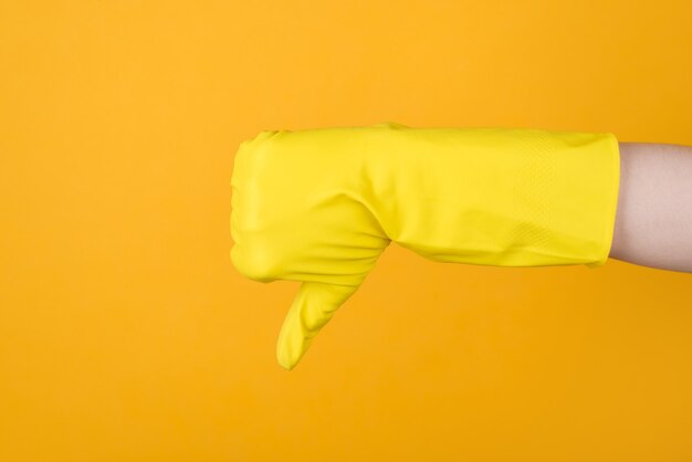 ハウスキーピングのコンセプト。黄色の背景に分離された親指ダウンサインを示す黄色の手袋の手のトリミングされた写真