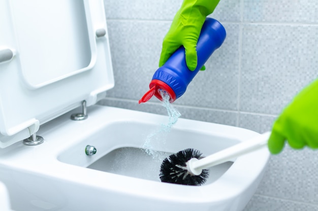 Housemaid in rubber gloves washing and disinfecting toilet using cleaning products and scrub brush. Household chores and cleaning service