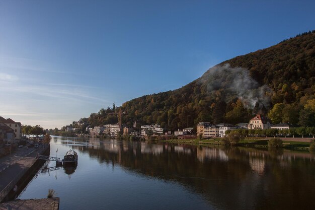 写真 天空を背景に木の山に沿った川岸の家