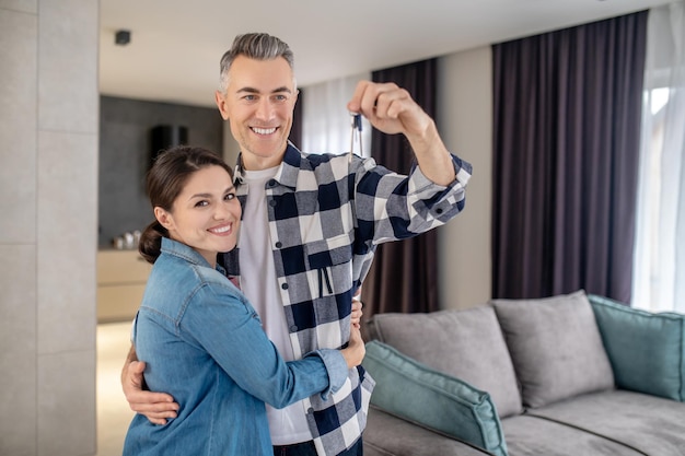 Housewarming Darkhaired joyful woman with husband holding keys in raised hand