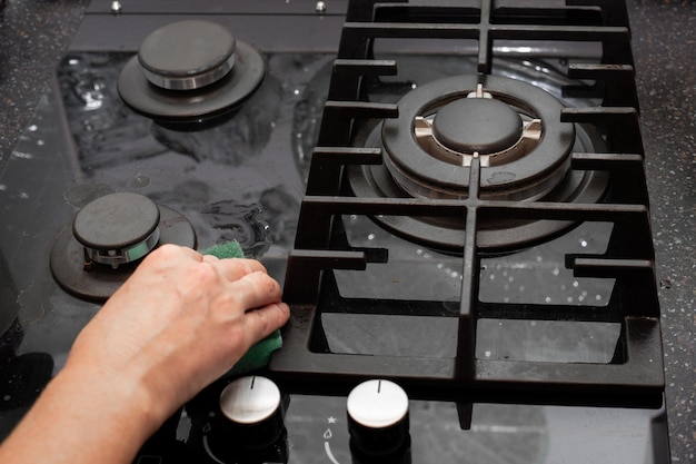 A housewife cleans the kitchen gas glassceramic black stove with a sponge House cleaning