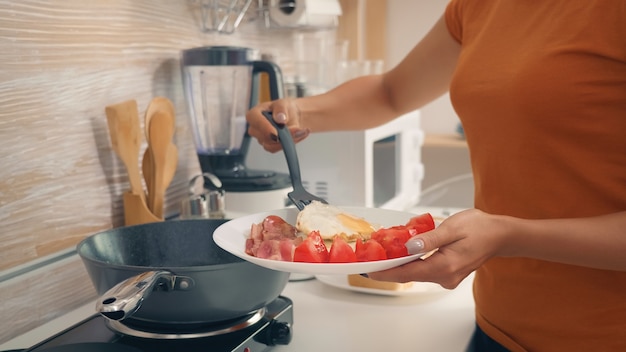 Casalinga che cucina le uova per la colazione in cucina. mattinata sana con prodotti freschi, stile di vita felice per la casalinga che cucina in un'accogliente cucina moderna sotto la calda luce del mattino estivo soleggiato