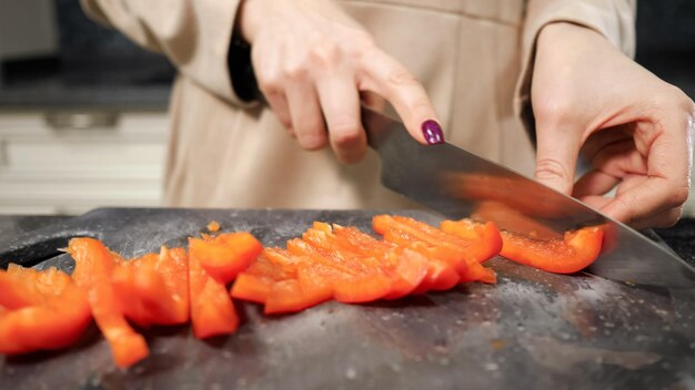 Домохозяйка режет болгарский перец на разделочной доске, делая салат