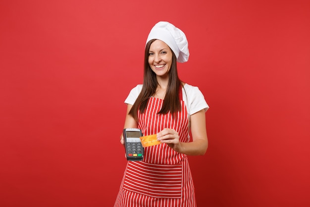 Cuoco o fornaio femminile della casalinga in cappello da cuoco unico del toque della maglietta del grembiule a strisce isolato sul fondo rosso della parete. la donna tiene in mano il dispositivo nfc della carta di credito del terminale di pagamento della banca mock up copy space concept