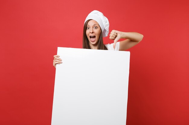 Housewife female chef cook baker in striped apron, white t-shirt, toque chefs hat isolated on red background. Woman hold big white blank billboard for promotional content. Mock up copy space concept.