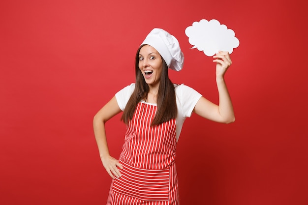 Housewife female chef cook or baker in striped apron white t-shirt toque chefs hat isolated on red wall background. Woman hold in hand empty blank Say cloud, speech bubble. Mock up copy space concept.