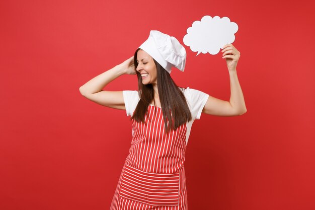 Housewife female chef cook or baker in striped apron white t-shirt toque chefs hat isolated on red wall background. Woman hold in hand empty blank Say cloud, speech bubble. Mock up copy space concept.