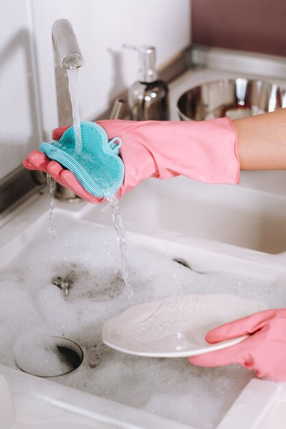 Housewife girl in pink gloves washes dishes by hand in the sink with detergent. The girl  washes dishes in gloves at home.