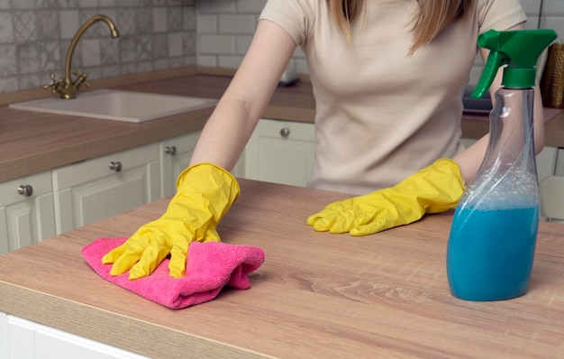 Housewife in gloves wipes dining table in kitchen Housework with cleaning products